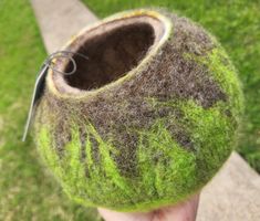 a hand holding up a green ball with grass on it