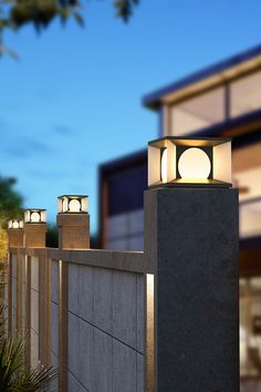 three lights are on top of a concrete block wall near a house at night with blue sky in the background