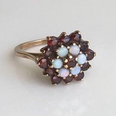 A vintage 9 carat yellow gold opal and garnet cluster ring. This beautiful piece holds a gorgeous collection of red and white stones in a gold setting. CONDITION: Wear consistent with age and use. All stones present. Please see photos for more detail. HALLMARKED 9 CARAT GOLD, ASSAYED IN LONDON 1973 SETTING DIAMETER: 16mm SETTING HEIGHT: 10mm BAND WIDTH: 1.5mm GARNET SIZE: 3mm (0.10ct) OPAL SIZE: 3mm (0.10ct) RING SIZE: UK: L 1/2 | US: 6 WEIGHT: 4.2 grams (UTZ) Garnet Gem, White Stones, Gold Signet Ring, Gold Engraving, Red Band, Aquamarine Rings, Multi Stone Ring, White Stone, Multi Stone