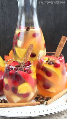 two glasses filled with fruit and cinnamon on a plate next to a pitcher of liquid