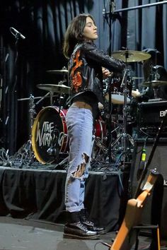 a woman standing on top of a stage next to a microphone and drum set in front of her