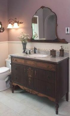 a white toilet sitting next to a wooden vanity in a bathroom under a large mirror