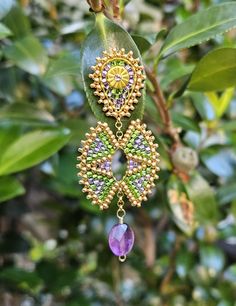 a pair of earrings hanging from a tree with leaves and flowers in the back ground