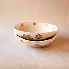 two white bowls with brown flower designs on them sitting side by side against a beige background