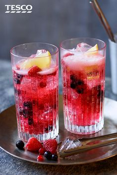 two glasses filled with ice and fruit on top of a metal tray next to silverware