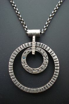 Silver Necklace - This Sterling Silver necklace is created using lost wax casting, fabrication and oxidization.  The two circles are able to rotate as you wear the necklace, and the smaller circle is adorned with a  sweet flush-set 1.5mm blue diamond.  A handmade clasp adds the finishing touch.  Each necklace is made by hand. Slight variation in size and patterning may occur. Please choose either a 16L or 18L chain. Hand Cast Minimalist Round Jewelry, Minimalist Hand Cast Round Jewelry, Spiral Metal Jewelry With Oxidized Finish, Modern Hand Forged Open Circle Jewelry, Modern Hand-forged Open Circle Jewelry, Unique Round Jewelry With Oxidized Finish, Hand Forged Spiral Jewelry For Anniversary, Elegant Circle Jewelry With Oxidized Finish, Elegant Circular Jewelry With Oxidized Finish