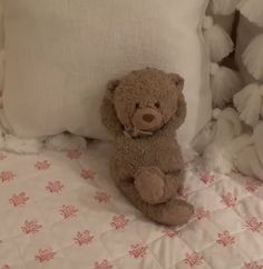 a brown teddy bear sitting on top of a bed next to white pillows and blankets