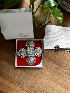 a red box with a silver cross on it next to a plant and an envelope