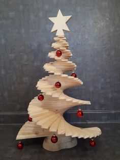 a wooden christmas tree with red and white ornaments on it's base, against a gray background