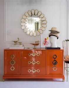 an orange dresser with gold accents and a mirror on the wall above it in a white room