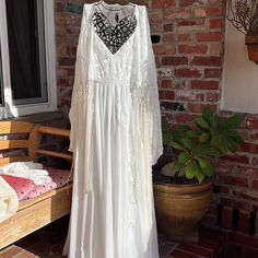 a white dress hanging on a brick wall next to a bench and potted plant