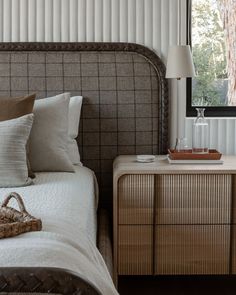 a bed sitting next to a wooden dresser under a window with a basket on top of it