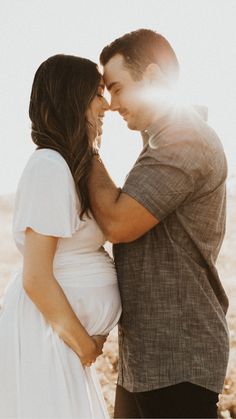 a man and woman standing next to each other in front of the ocean with sun shining on them