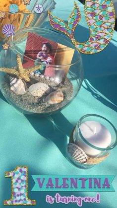 a vase filled with sand and shells on top of a blue table cloth next to a candle