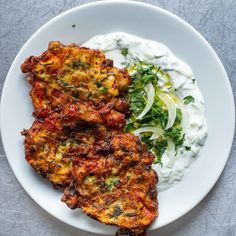 two fritters on a plate with sour cream and greens