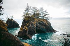 an island with trees on top of it near the ocean and some rocks in the water