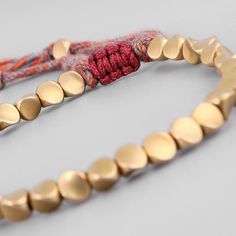 two bracelets with gold discs and red string on grey background, close up photo