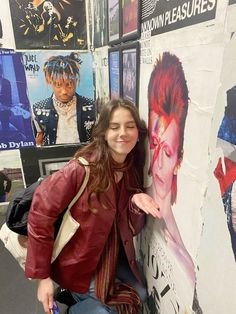 a woman leaning against a wall with posters on it