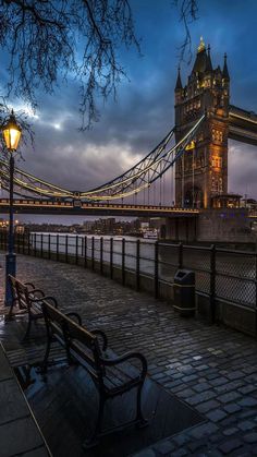 a bench sitting on the side of a river next to a tall tower with a bridge in the background