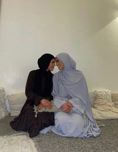 two women in hijabs sitting on the floor next to each other and looking at each other