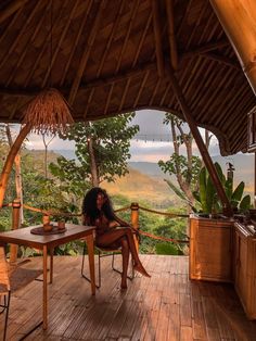 a woman sitting at a table on top of a wooden deck next to a forest