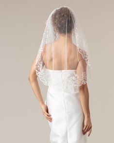 the back of a bride's wedding dress with a veil on her head and shoulders