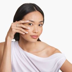 a woman in white shirt holding her hand to her face and looking at the camera