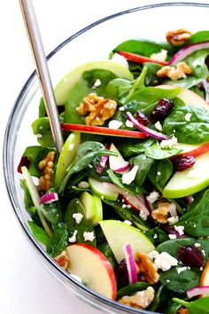 a salad with spinach, apples, walnuts and feta cheese in a glass bowl