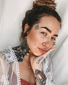 a woman with tattoos on her face and neck posing for the camera while laying down