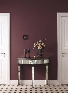 a table with flowers and candles on it in front of a purple painted wall, next to a white door