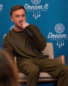 a man sitting in a chair holding a microphone up to his mouth as he speaks