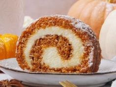 a cinnamon roll sitting on top of a white plate next to oranges and other autumn decorations