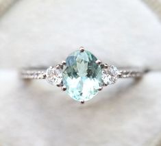 an aqua and white diamond ring sitting on top of a piece of paper