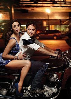 a man riding on the back of a motorcycle next to a woman in a blue dress