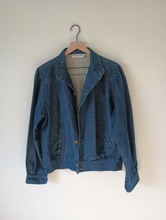 "Vintage 1980s classically styled dark denim jacket. Great 80's  silhouette.  Wide band collar can be worn standing up, or folded down. Brass snap closures, front and cuffs.  Pleated shoulders, front and back yoke.  two front slant poclets/  Wide band, elasticized  at back, clean and flat at front edge, hip length. Additional subltle pleat detail at hem.  Dark denim wash, 100% cotton, outstanding condition.  Made in  Dubai.  Labeled Bermuda Run.  Gender neutral, check measurements, fits a modern Dark Denim Jacket, Blouson Jacket, Band Collar, Dark Denim, Hip Length, Denim Wash, In Dubai, Modern Woman, Stranger Things