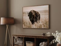 a bison standing in the middle of a field with tall grass and flowers next to it