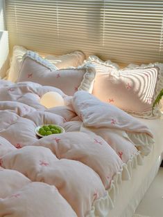 a bed with pink and white sheets, pillows and a bowl of food on it