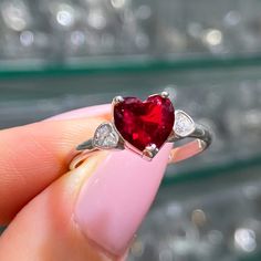 a woman's hand holding a heart shaped ruby and diamond ring