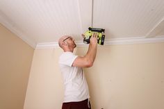 a man in white shirt and red shorts working on a ceiling with a driller