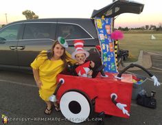 a woman standing next to a child in a car costume with the cat in the hat on