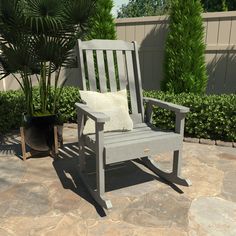 a wooden rocking chair sitting on top of a stone floor next to a potted plant