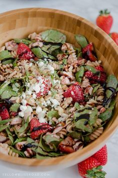 a wooden bowl filled with salad next to strawberries