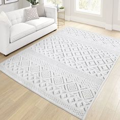 a living room with white furniture and wood flooring, including a rug on the floor