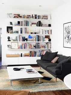 a living room filled with furniture and bookshelves next to a wall mounted book shelf