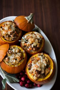 four stuffed pumpkins on a plate with cranberries and other food items around them