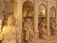 some statues are sitting on the side of a wall in front of a shelf filled with books