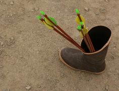 a pair of brown boots with green arrows sticking out of them on dirt ground next to rocks