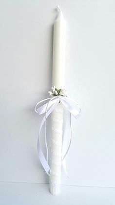 a white candle with a ribbon tied around it on a wall next to a flower