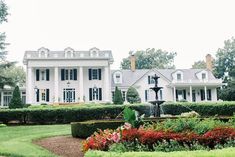 a large white house sitting in the middle of a lush green field next to a garden