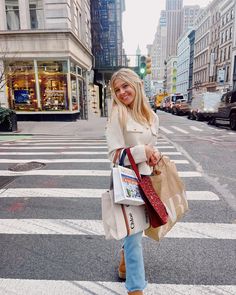 a woman is walking across the street with shopping bags in her hand and she is smiling at the camera